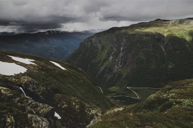 A green mountain valley with patches of snow under heavy cloud, in DSTY G 800