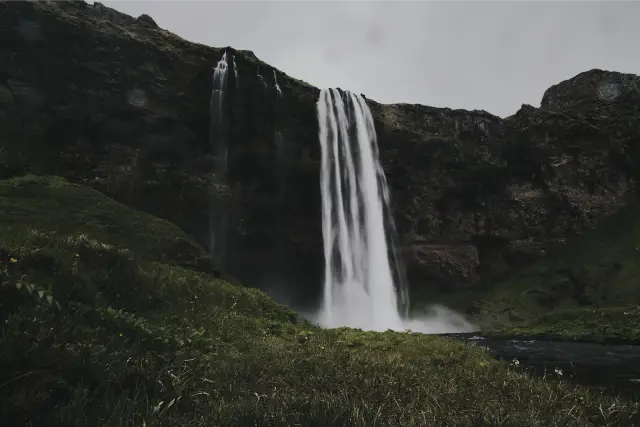 A tall waterfall dropping over a green cliff in Iceland, in DSTY G 800