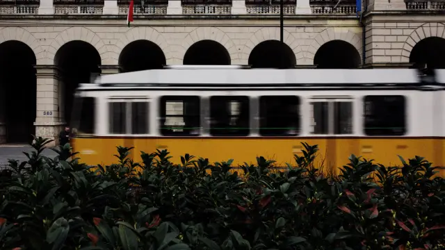 A yellow tram passing a stone arcade in Budapest, in VNTG 800