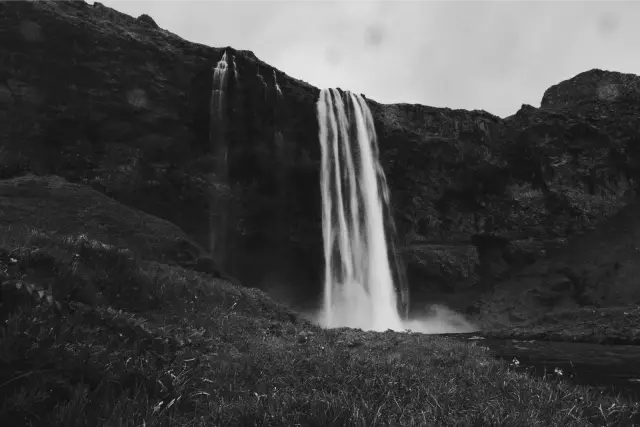 A tall waterfall dropping over a green cliff in Iceland, in Ilford Delta 3200