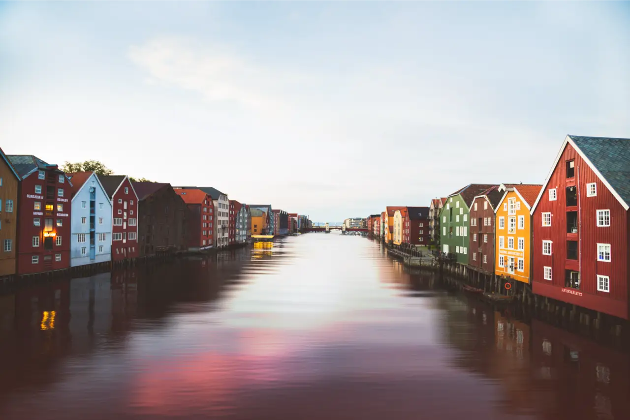 Painted wooden warehouses along a calm river in Trondheim, unedited