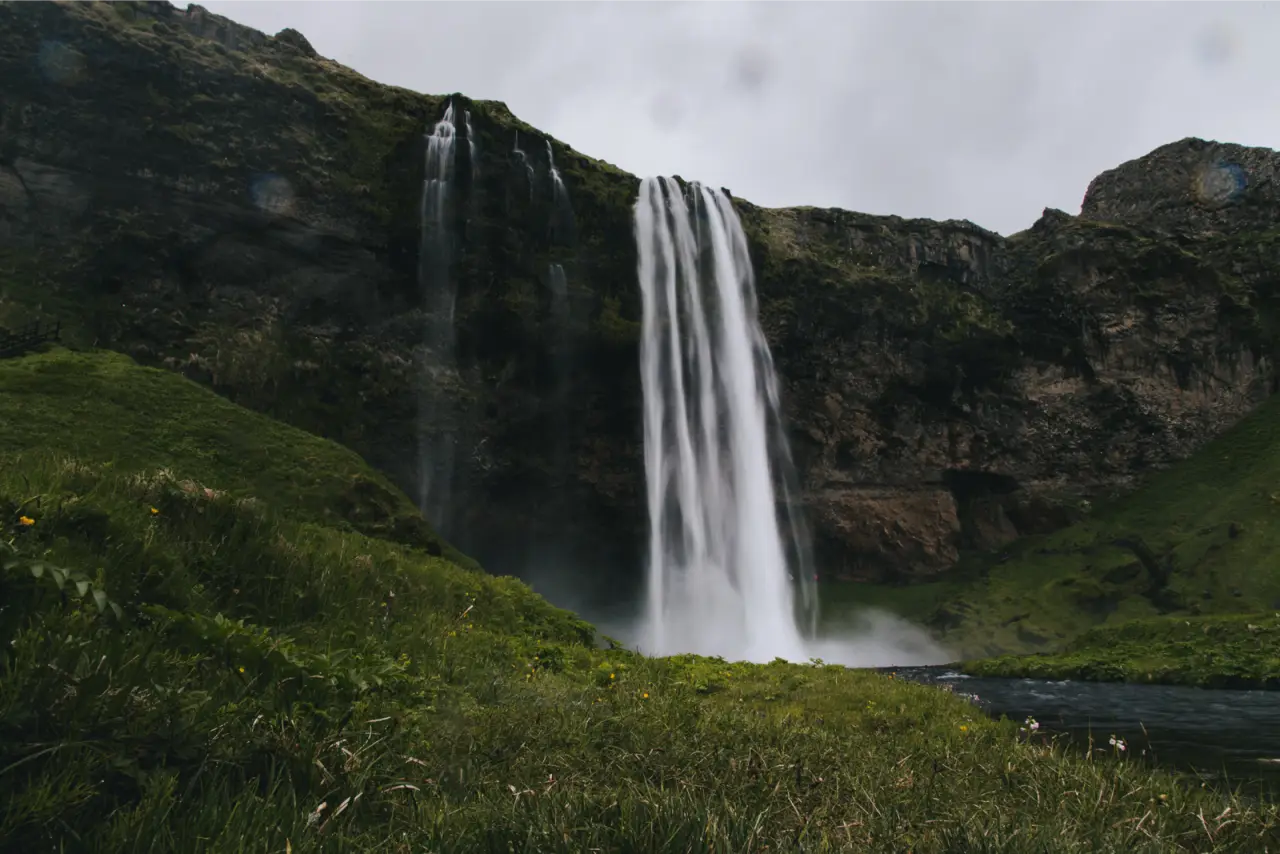 A tall waterfall dropping over a green cliff in Iceland, unedited