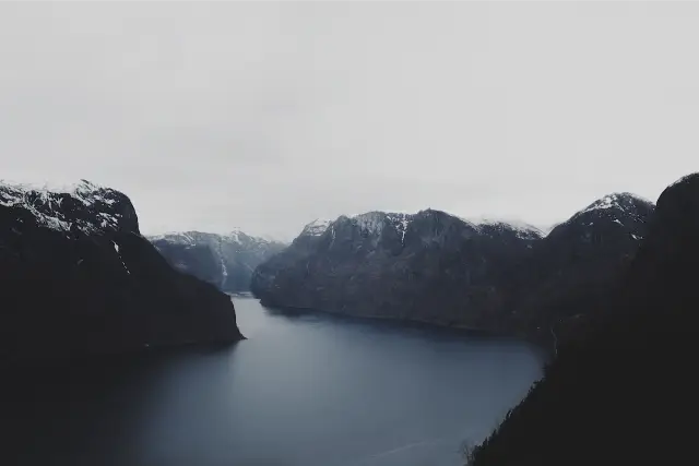 A dark blue fjord between snow-topped mountains, in SVAL C 100