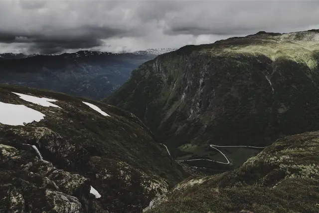 A green mountain valley with patches of snow under heavy cloud, in SVAL C 100
